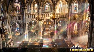 Seen from above, a cathedral fills with colored sunbeams across rows of pews