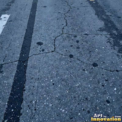 Asphalt pavement marked with oil stains and tire scuffs in medium gray