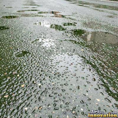 Wet asphalt glistening with small puddles in a greenish gray tone