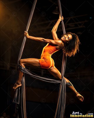 Split midair on aerial silks, a woman in an orange bodysuit smiles in a dim hall