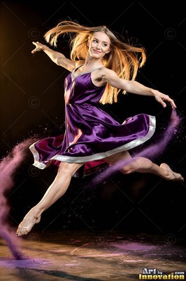 A smiling woman leaps in a purple satin dress with violet powder swirling past her feet
