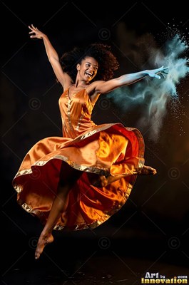 Leaping in the air, a smiling woman in an orange dress scatters blue powder