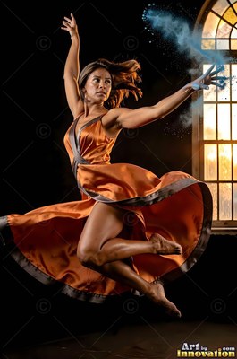Woman in an orange dress leaping as blue powder bursts from her hand