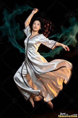 A woman jumps in a silver satin robe with smoky teal trails curling behind her
