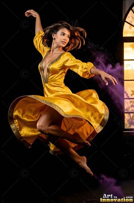A woman springs through the air in midair wearing a swirling yellow dress beside purple powder cloud