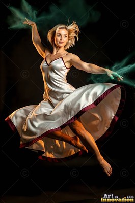 In a dark room, a barefoot woman in a white satin dress leaps with green powder flying