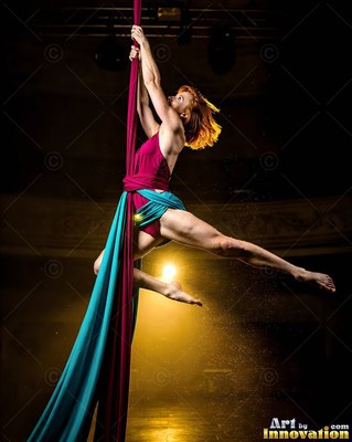 Woman hanging from red and blue aerial silks in warm stage light