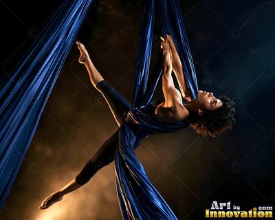 Suspended sideways in midair, a woman stretches between blue silks in soft light