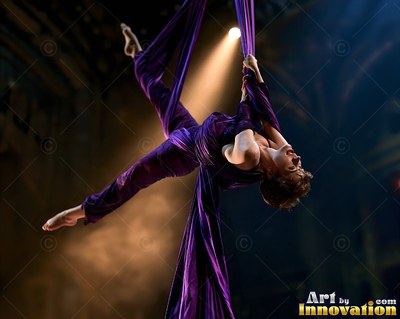 Hanging upside down from purple silks, a woman bends back under a spotlight