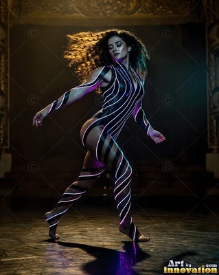 Woman dancing on a dark stage in a suit of pink neon stripes