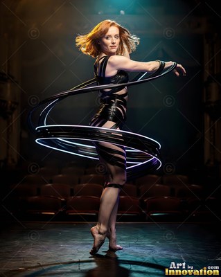 On a dark stage, a red-haired woman dances inside spirals of white streaks of light
