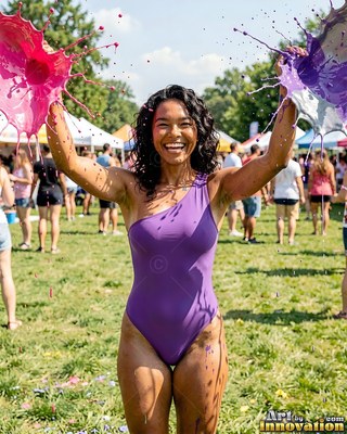 Wearing a purple one-shoulder swimsuit, a happy woman is hit with paint with paint on a sunny lawn
