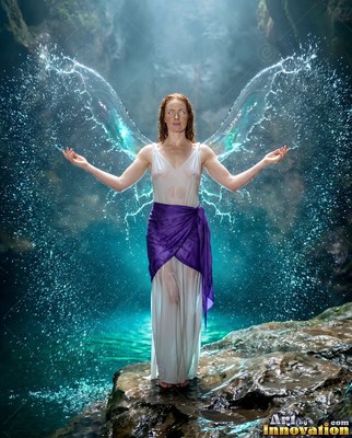 A woman in a white dress stands with wings made of water splashing