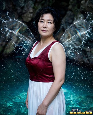 Standing by blue water, a dark-haired woman wears splash wings and a red dress