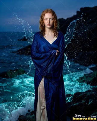 A woman stands by the rocky sea with wings of water, lit by bright turquoise surf