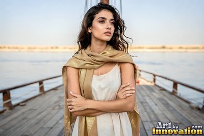 Woman on the open deck of a felucca on the Nile, a linen scarf around her shoulders and the far bank a thin gold line behind her