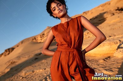 On desert dunes, a woman in a sleeveless rust jumpsuit poses in the sun