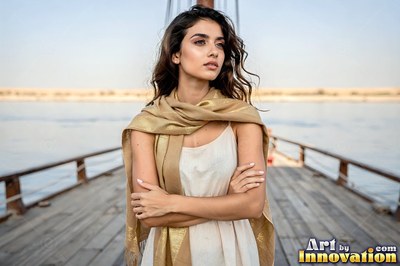 On a wooden boat, a young woman folds her arms wearing a gold scarf