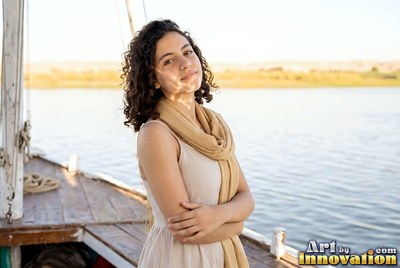A tan scarf rests on a smiling young woman standing on a wooden boat on the Nile river