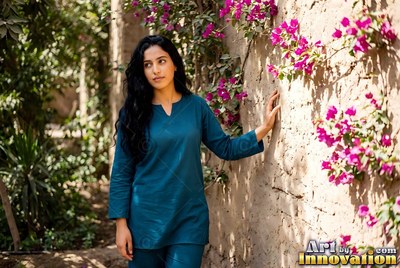 Along a garden path, a woman in a blue tunic touches a mud wall by pink flowers