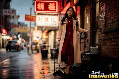 A woman walks down brownstone steps in a tan trench coat under red neon city signs