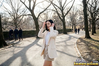 Walking forward in Central Park, a smiling woman in a beige blazer touches her hair