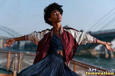 On a rooftop near a bridge, a woman poses with arms wide in a satin jacket