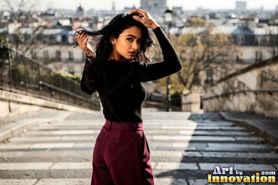 Touching her hair, a woman in maroon pants looks back on stone steps in Paris