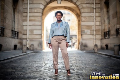 A woman in a light blue jacket stands under a stone archway