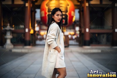 Standing outside a temple gate, a woman in a long cream cardigan looks back