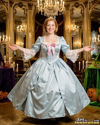 Cheerful woman in a light blue ballgown standing with open arms in a ballroom