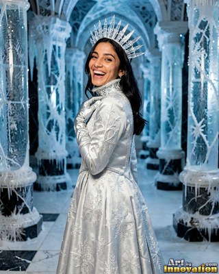 Wearing a pointed ice crown, a cheerful woman in a silver gown poses by frozen pillars