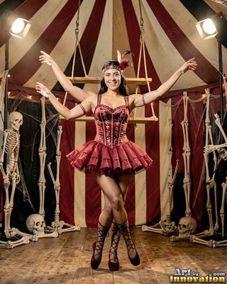 A happy woman poses with four arms under bright stage lights in a red circus outfit