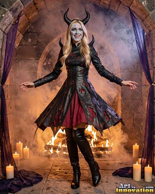Woman in a horned devil costume smiles near a stone fireplace