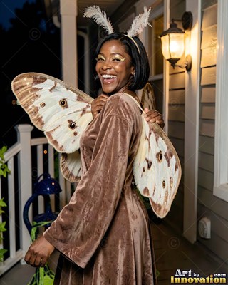 Feather antennae top a woman smiling in a moth costume on a front porch at night