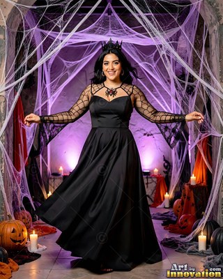 Standing front and center, a happy woman in a black gown poses among cobwebs