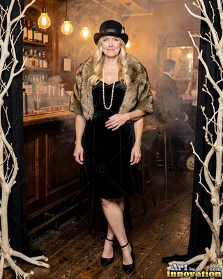 A happy woman poses in a black velvet dress and fur stole under warm yellow lights