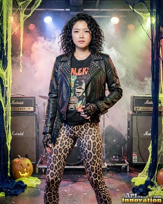 A woman stands in a rock costume on a stage with soft colorful lighting