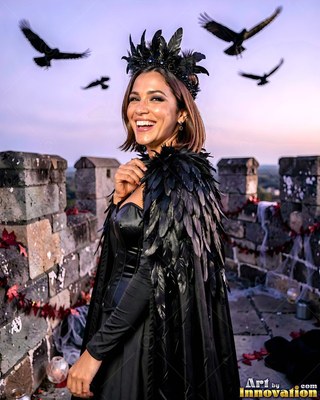 Black feather headpiece on a woman smiling standing on a stone castle tower as birds fly