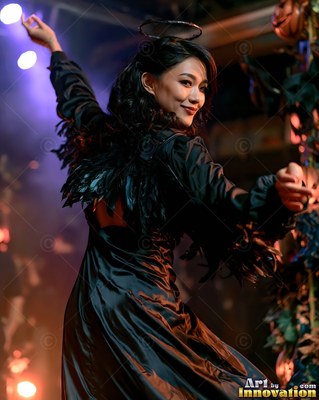 A woman in a black fallen angel costume dances under purple stage lights