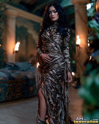 A woman in a brown mummy wrap dress stands in a dim tomb lit by torches