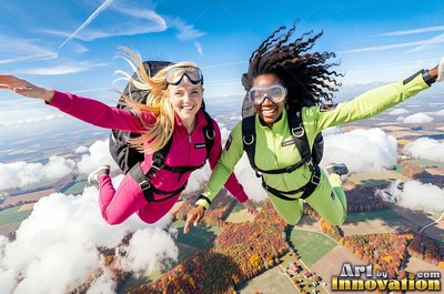 In the bright sky above clouds, two smiling women skydive in pink and green jumpsuits