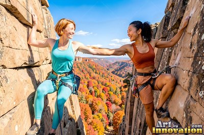 Holding hands while rock climbing, two smiling women look across a sunlit canyon gorge
