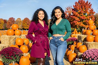 Two woman friends smile together in a pumpkin patch under bright sunlight