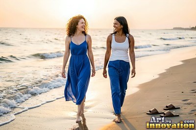 Two smiling women walk barefoot on a sandy beach in warm evening sunlight