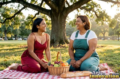Two adult women laugh together during a sunny park picnic under a tree