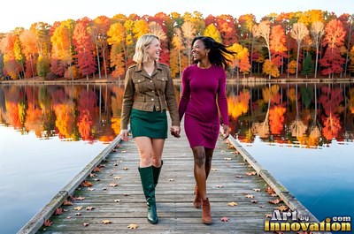 On a wooden dock by an autumn lake, both women walk hand in hand and smile