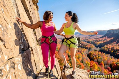 Dressed in pink and lime athletic wear, two women climb a cliff above fall trees