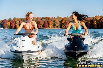 Two women travel on jet skis across a lake in bright sunlight before colorful fall trees