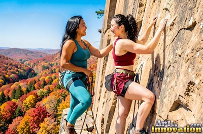 Rock climbing together, two smiling women pause on a sunny cliff over autumn hills